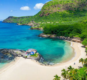 Bucht mit weißem Sandstrand, türkisfarbenem Wasser und grün bewachsenen Hügeln auf den Kapverdischen Inseln unter blauem Himmel.