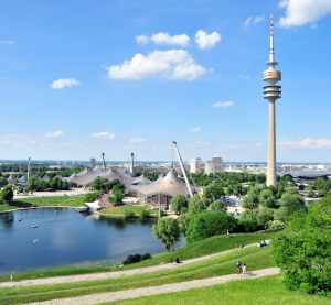 Blick auf den Olympiapark und Fernsehturm in M&uuml;nchen bei blauem Himmel. 