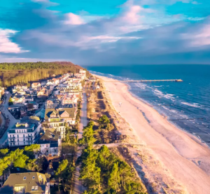 Luftaufnahme einer deutschen Ostseeinsel mit Sandstrand, Strandpromenade, K&uuml;stenwald und H&auml;usern im Abendlicht.