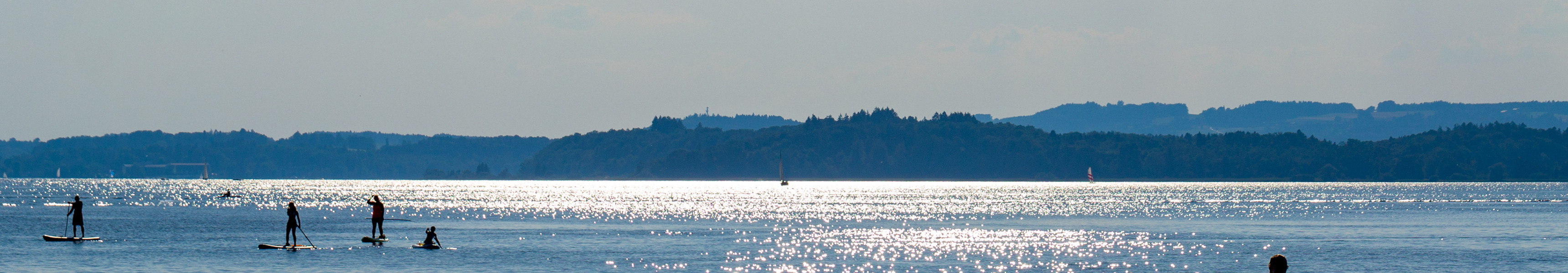 Blick auf den Chiemsee mit Alpenkulisse und Stand-Up-Paddler auf dem Wasser