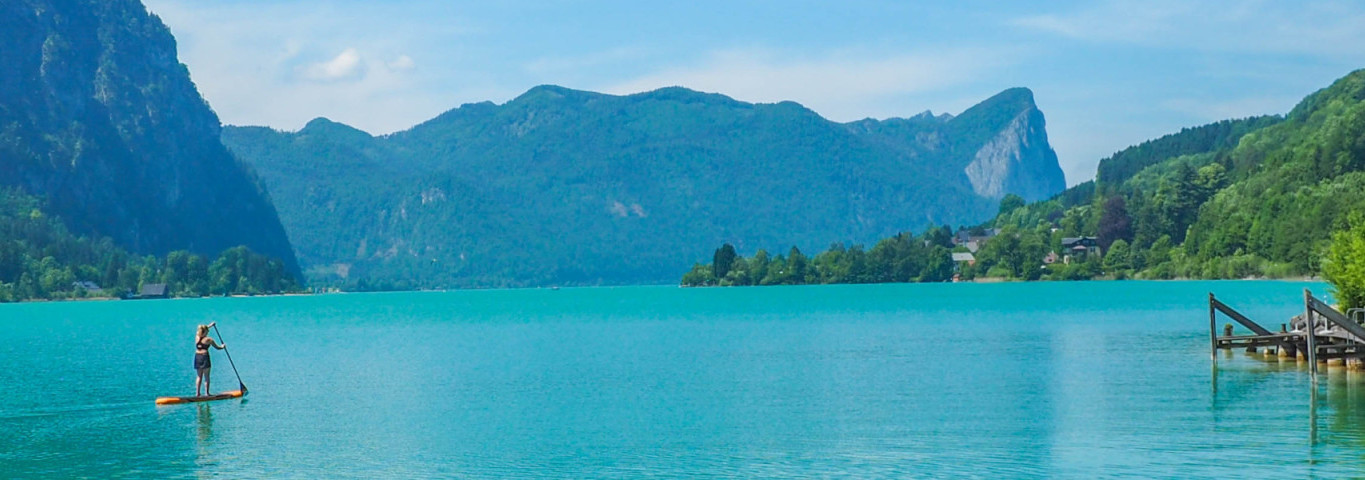 Panoramablick auf den türkisblauen Wolfgangsee in Österreich mit Bergen, Steg und Stand-up-Paddler